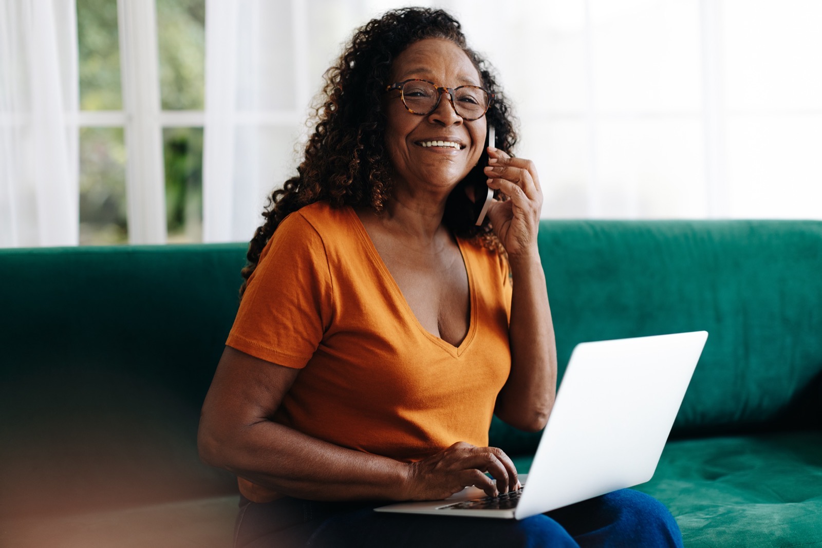Woman wearing glasses, smiling on the phone with a laptop while enrolling in a VSP vision plan from home